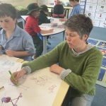 A woman in a green jumper is drawing an image of Australian wildlife while a young boy watches.