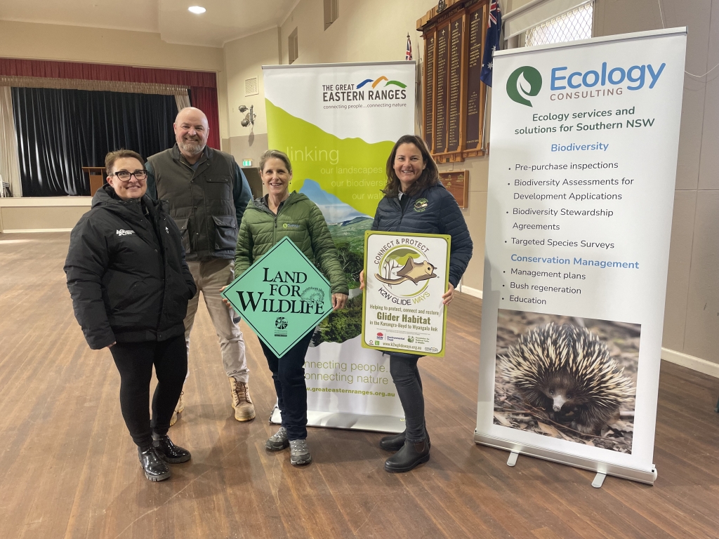 Three women and a man are standing in front of signs that read Ecology Consulting and Great Eastern Ranges holding signs for Land for Wildlife and K2W Link Inc.