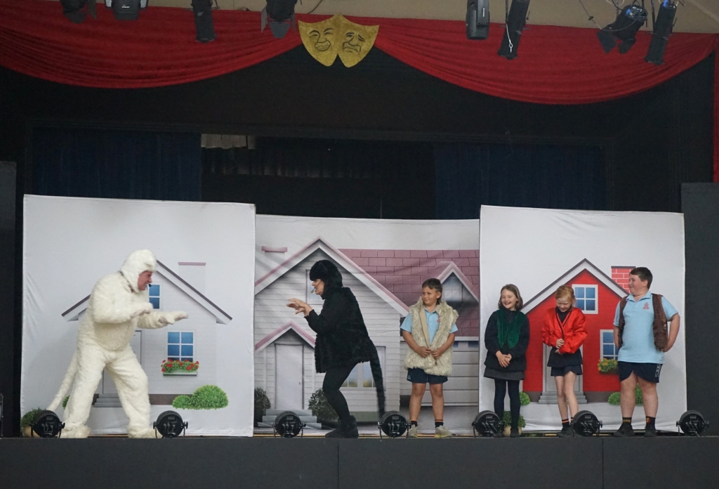 Two performers dressed as cats and four primary-school aged children perform on-stage.